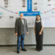 Dr. Friedemann Burkhardt steht gemeinsam mit einer Frau vor einer Wandgrafik an der Handong Global University in Südkorea. Auf der Grafik sind die Worte ‚Honesty, Integrity and Faith‘ zu lesen