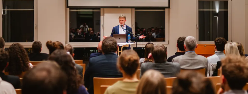 Thomas Kleber hält seine Antrittsvorlesung im Atrium des Missions- und Schulungszentrums in Bad Liebenzell. im Vordergrund ist eine große Menschenmengen, die fokussiert seinem Vortrag zuhört.