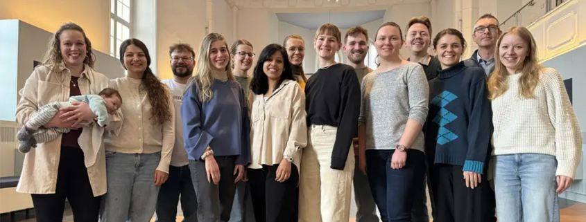 Eine 15-köpfige Gruppe aus ehemaligen Studierenden ist lächelnd auf einem Gruppenfoto zu sehen